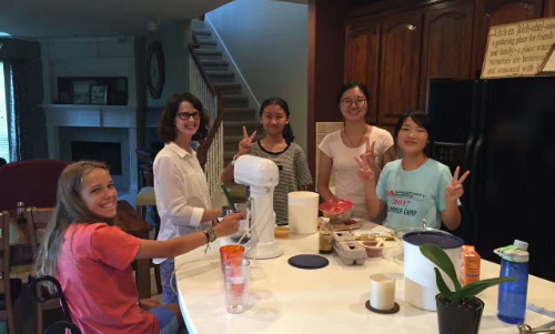 Students and a host parent gathered around a kitchen island preparing food together.