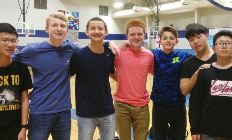 A group of seven high school students posing together in a school gymnasium.